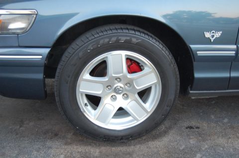 1985 Mercury Grand Marquis - Close-up of a silver five-spoke wheel and red brake caliper on a blue vehicle.