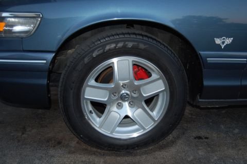 1985 Mercury Grand Marquis - Close-up of a car's wheel and fender, showing a silver five-spoke wheel with red brake calipers.