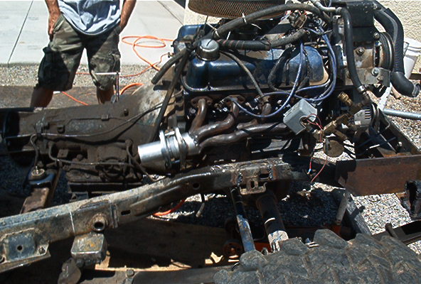 Engine and transmission assembly on a vehicle frame. A person stands in the background