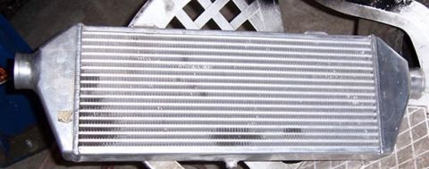 1988 Pontiac Fiero - An aluminum intercooler with silver fins and black end tanks is shown, with visible text on the lower right corner.