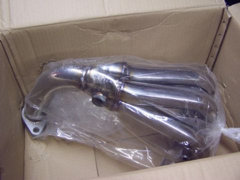 2000 Ford Crown Victoria - A shiny exhaust manifold is shown packaged in plastic within a cardboard box.
