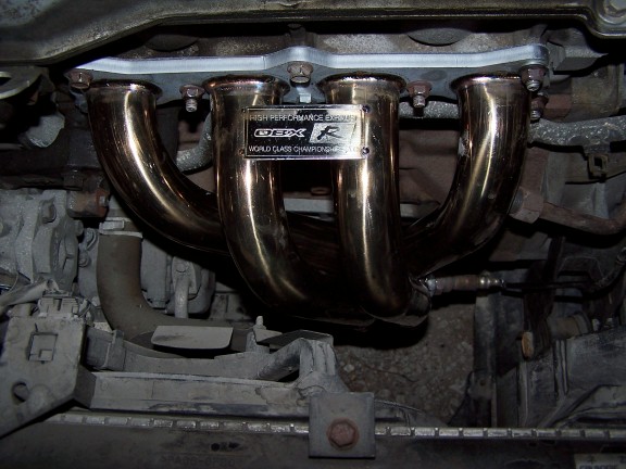 Aftermarket exhaust manifold with 'OBX R' and 'World Class Championship' text on a metal plate
