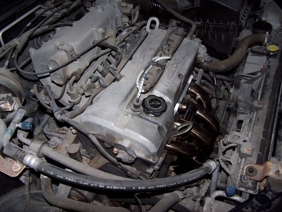 Mazda engine with exhaust manifold and hoses. The engine cover has "MAZDA" text