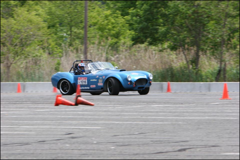 Blue convertible race car with roll bar and racing decals on side, driving on asphalt track with orange cones