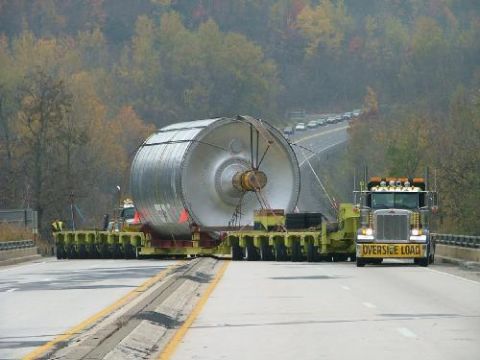 1979 Ford Bronco - A large industrial component is transported on a multi-axle trailer, led by a Peterbilt truck, with a line of cars following on the highway.