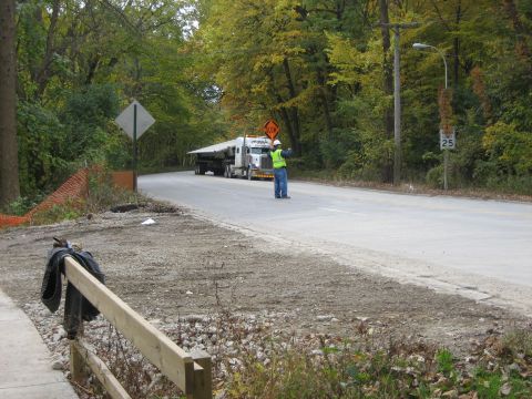 1979 Ford Bronco - A semi-truck transports a long load down a road while a worker directs traffic.