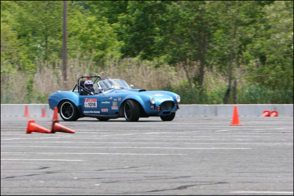 Blue convertible race car with roll cage and racing decals on a track, driver wearing helmet