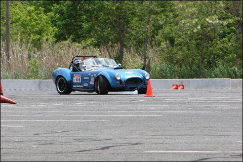 2001 Mercury Grand Marquis - Blue AC Cobra replica navigates a race track, marked by orange cones and racing decals.