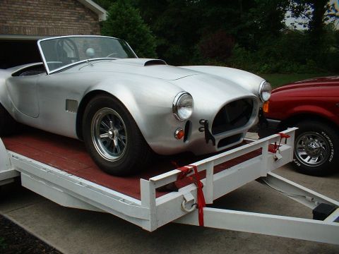 1965 Shelby Cobra - A silver 1965 Shelby Cobra is loaded onto a trailer, with a red truck visible to the right.