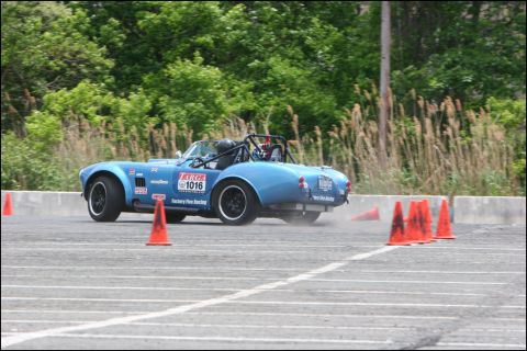 2001 Mercury Grand Marquis - A blue convertible sports car with racing decals navigates an autocross course, kicking up dust.
