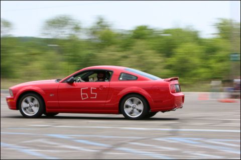 2001 Mercury Grand Marquis - Red Ford Mustang GT races on a track, showing its side profile and number 65.