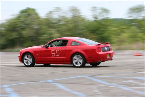 2001 Mercury Grand Marquis - A red Ford Mustang GT is captured in motion on a race track, with the number 65 visible on its side.