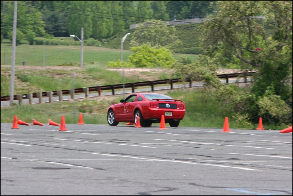 Red Ford Mustang coupe with number 65 on door, driving on asphalt track with orange cones