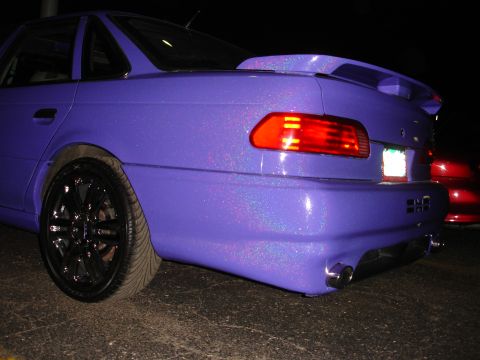 1993 Ford Taurus - The rear quarter panel of a custom purple sedan is shown, a spoiler and dual exhaust pipes.