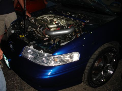 1993 Ford Taurus - The engine bay of a blue car is open, revealing aftermarket modifications.