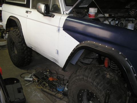 1966 Ford Bronco - Driver's-side view of an early Ford Bronco mid-build in a garage, white body with a dark navy front fender and hood, showing freshly fitted…