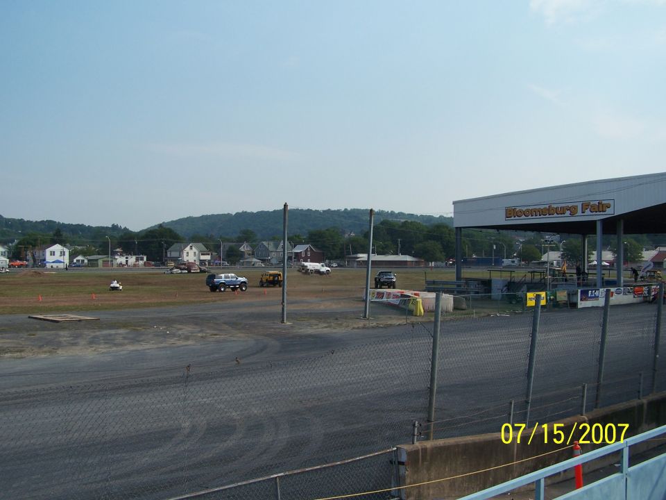 Several SUVs and a yellow vehicle are parked on a dirt field near a grandstand