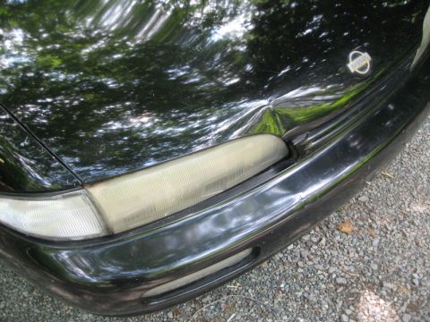 1995 Nissan 240SX - Close-up of a black car's front corner, showing the Nissan badge and headlight assembly.