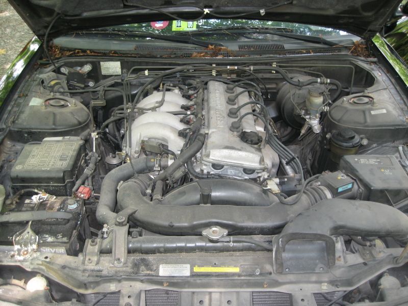 Engine bay of a Nissan vehicle, showing the V6 engine, fuse box, and battery