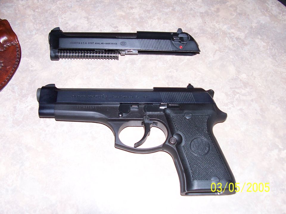 Black Beretta pistol disassembled into frame and slide on a countertop