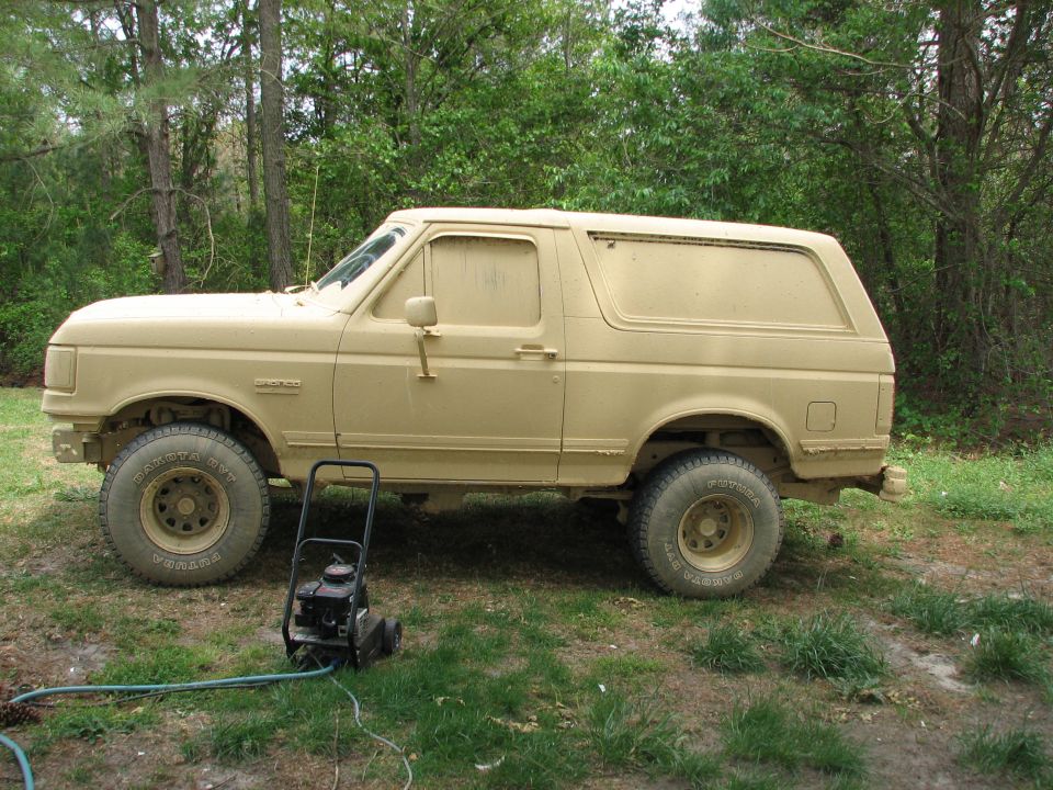 Mud-covered two-door SUV in side view with pressure washer in front, parked on grass.