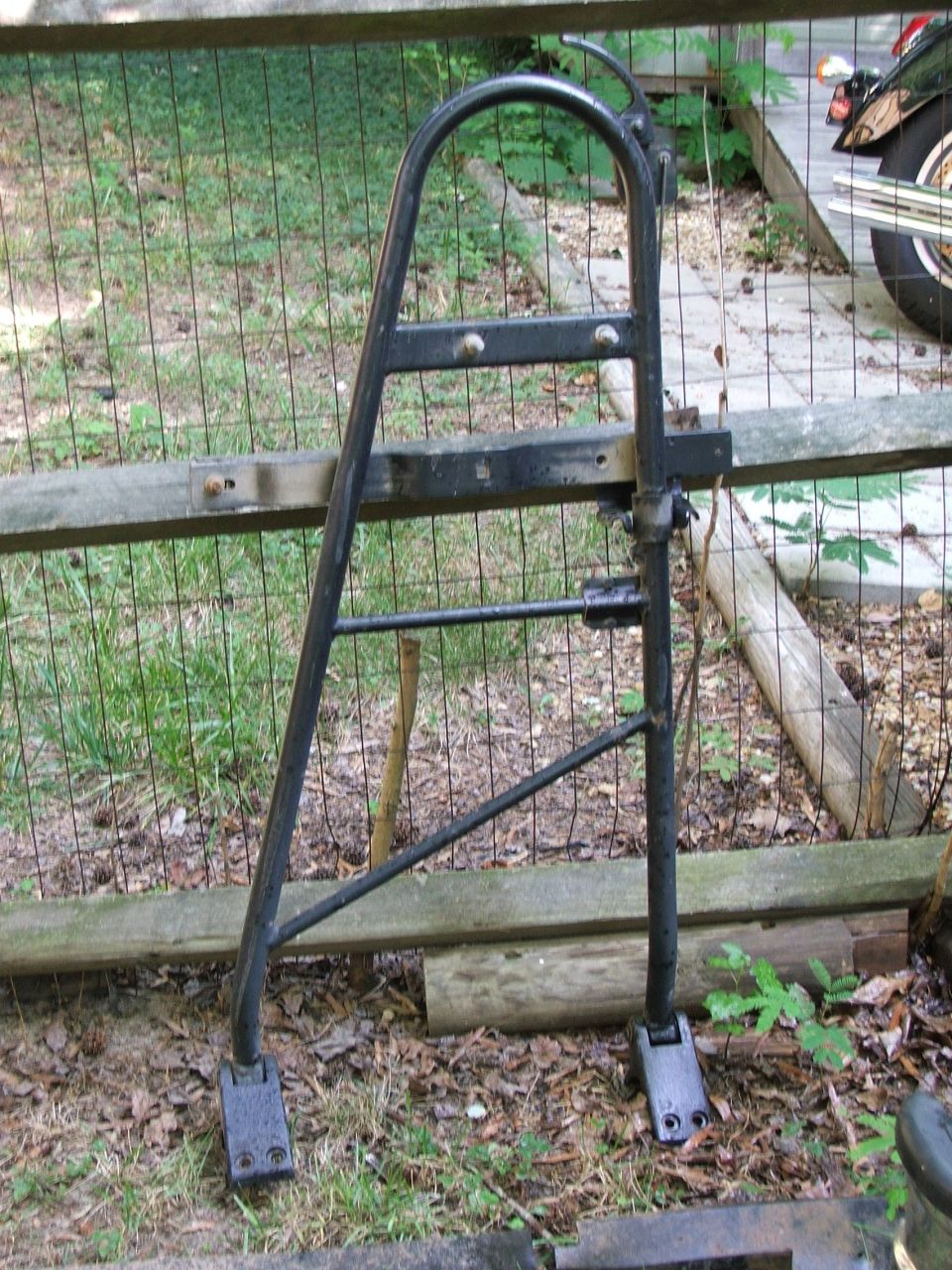 Motorcycle luggage rack leaning against a fence, with a motorcycle wheel visible to the right