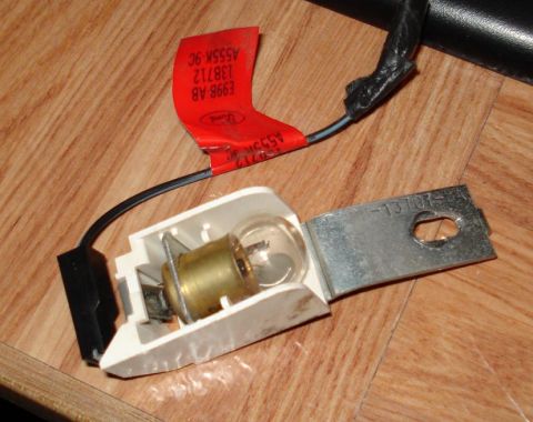 1999 Ford Crown Victoria - An under-dash courtesy light assembly lying on a wood surface: a white plastic housing holding a clear brass-based bulb, a zinc-plated moun…