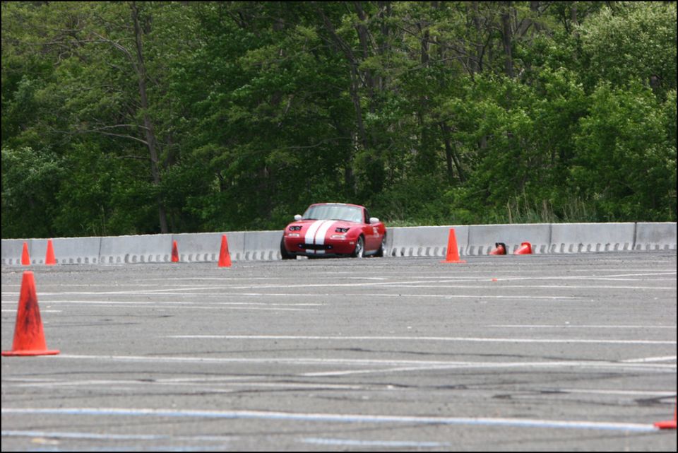 Red convertible with white stripes on track with orange cones
