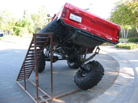 1970 Ford Bronco - A heavily modified red truck is positioned on a metal ramp, its off-road capabilities.
