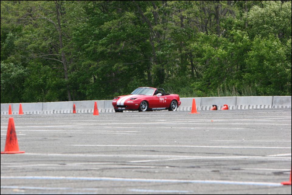 Red convertible sports car with white stripes and number 11 on the door, seen from the front-right at an autocross event