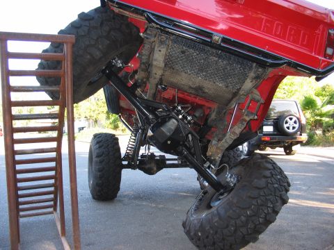 1970 Ford Bronco - This modified 1970 Ford Bronco is shown with its chassis elevated on a ramp, highlighting its robust undercarriage and large off-road tires.