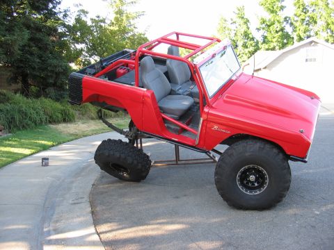 1970 Ford Bronco - Modified 1970 Ford Bronco with custom roll cage and large off-road tires is shown in a driveway.