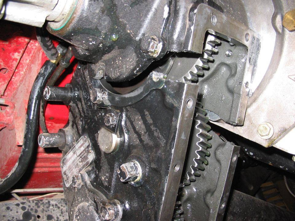 Close-up of black engine block with exposed gears and bolts, red metal visible on the left