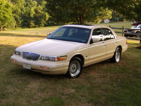 1996 Mercury Grand Marquis - A tan sedan sits on a grassy lawn under trees, viewed from the front three-quarter angle.
