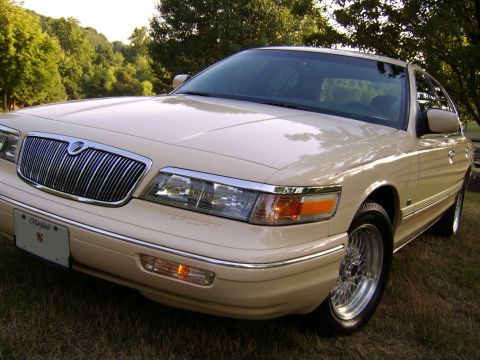 1996 Mercury Grand Marquis - A cream-colored 1996 Mercury Grand Marquis is parked on grass with trees in the background.
