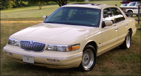 1996 Mercury Grand Marquis - A tan sedan is parked on a grassy lawn with trees in the background.
