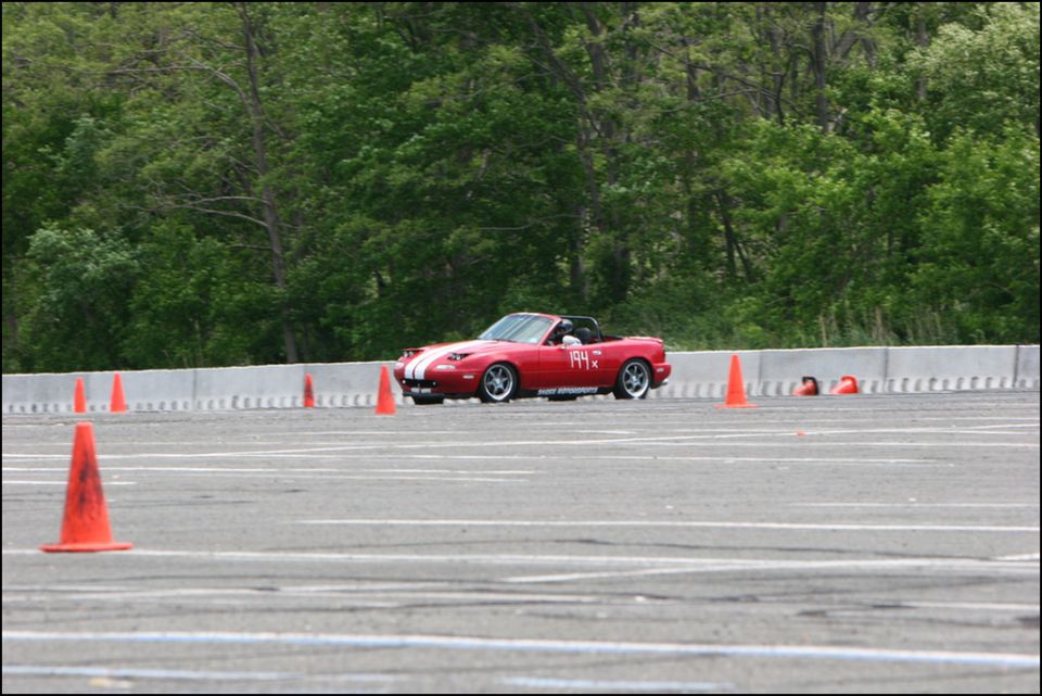 Red Mazda Miata convertible with white racing stripes and number 194X on the door, on a paved track with orange cones