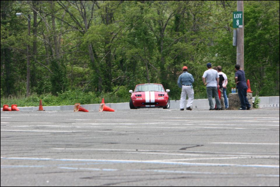 Red sports car with white stripes on track, people watching. Lot 8 sign visible