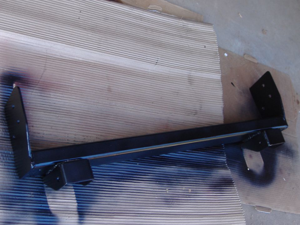 Black-painted steel crossmember with mounting brackets on cardboard