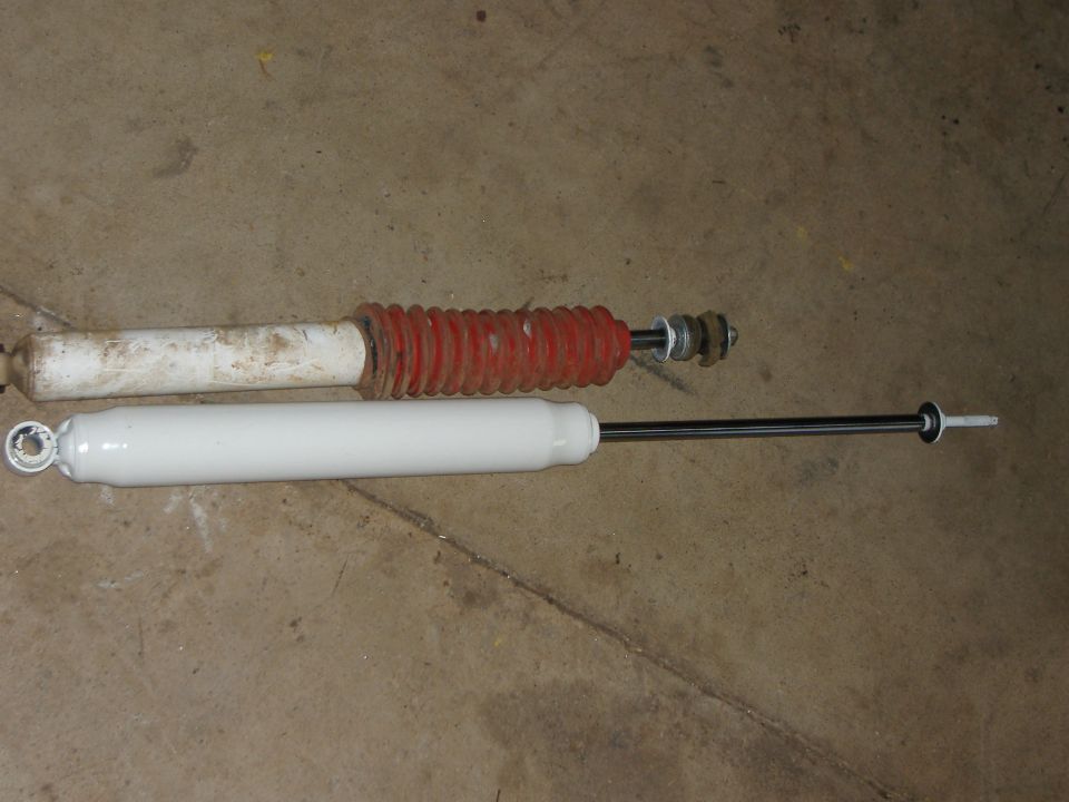 Two shock absorbers, one with red boot, lying on a concrete floor