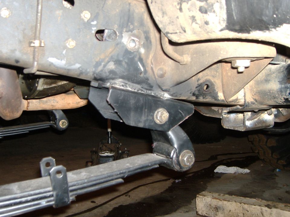 Underside of Bronco showing black leaf spring hanger and shackle mount on frame with leaf spring and jack below