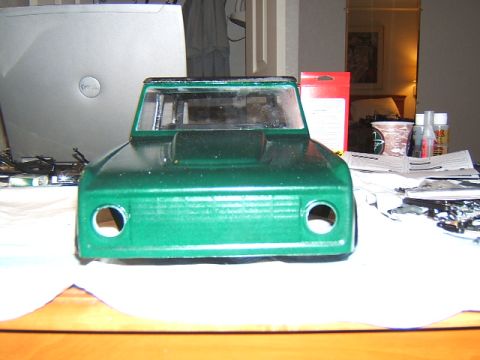1988 Ford Bronco - This is a front view of a green RC car body, likely a model kit, placed on a table with various craft supplies and a laptop in the backgrou…