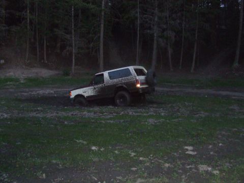 1990 Ford Bronco - A muddy 1990 Ford Bronco navigates a challenging off-road terrain, with its spare tire mounted on the rear.