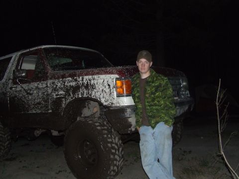1990 Ford Bronco - Man stands next to a heavily mud-splattered 1990 Ford Bronco in the dark.
