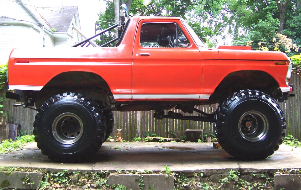 Orange lifted 1978 Ford Bronco with large off-road tires and roll cage, side view