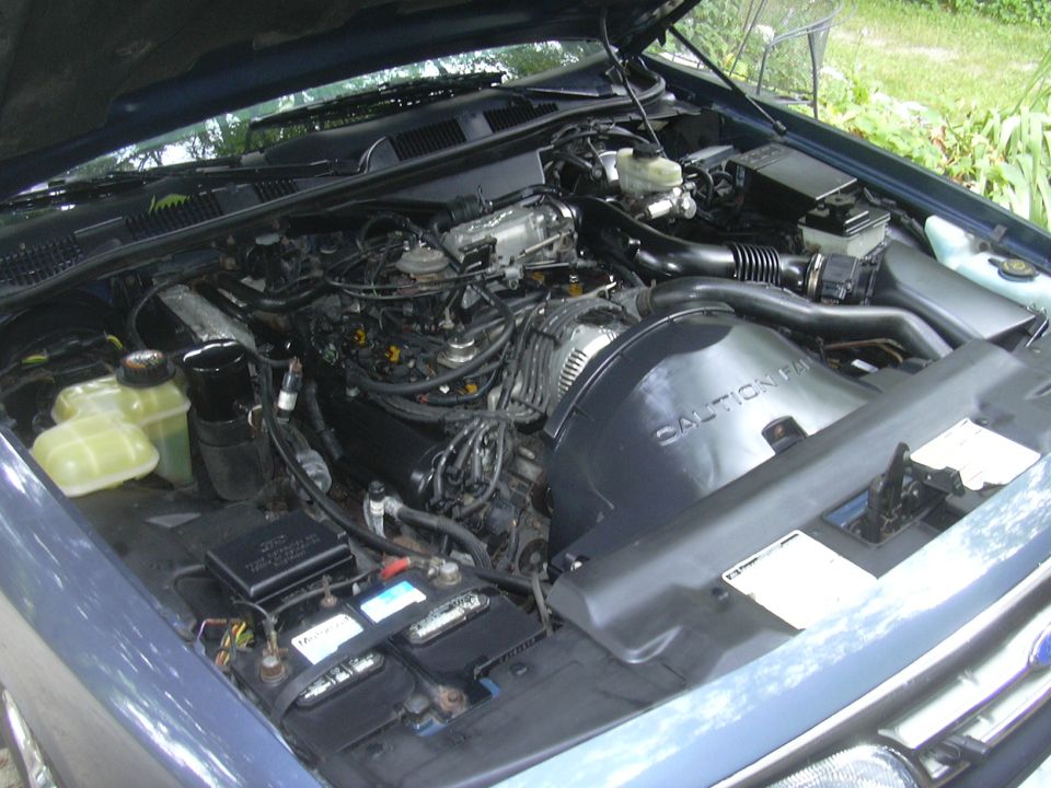 Blue car engine bay with hood open, showing engine components, battery, and coolant reservoirs