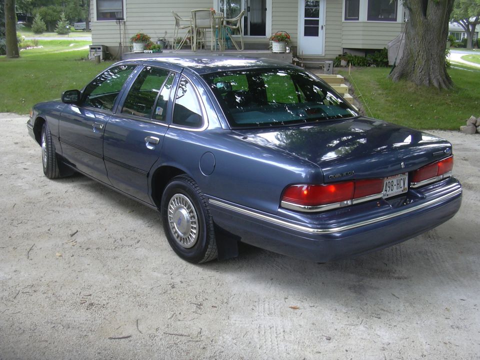 1996 Ford Crown Victoria, rear 3/4 view, blue paint, parked on gravel driveway
