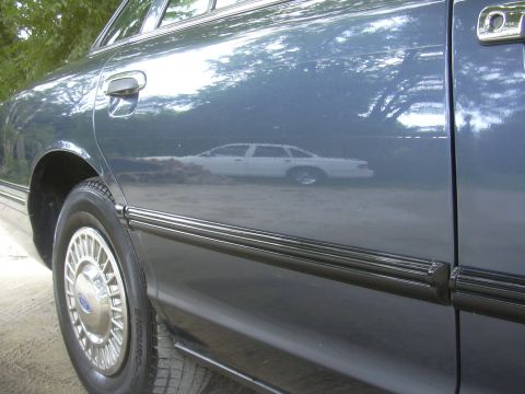 1996 Ford Crown Victoria - Reflection of a white car is visible on the side of this blue 1996 Ford Crown Victoria.
