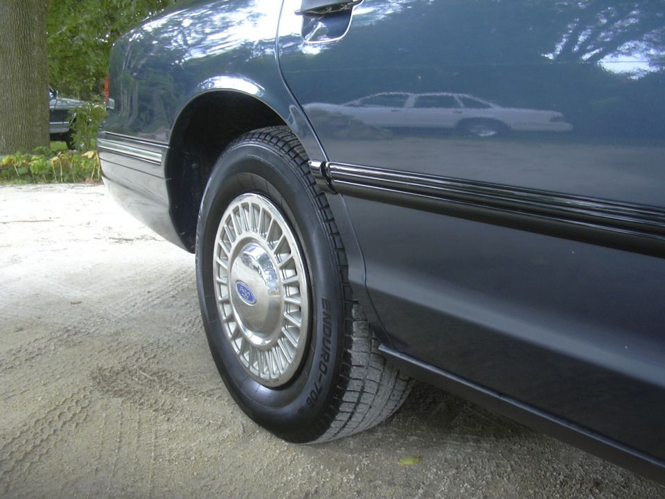 1996 Ford Crown Victoria side view, dark blue sedan rear quarter panel and wheel with chrome hubcap