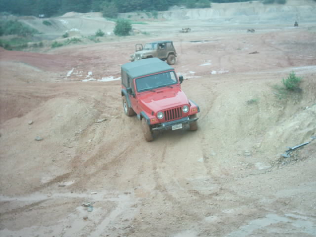 Red 2003 Jeep Wrangler driving on a dirt hill with another Jeep in the background